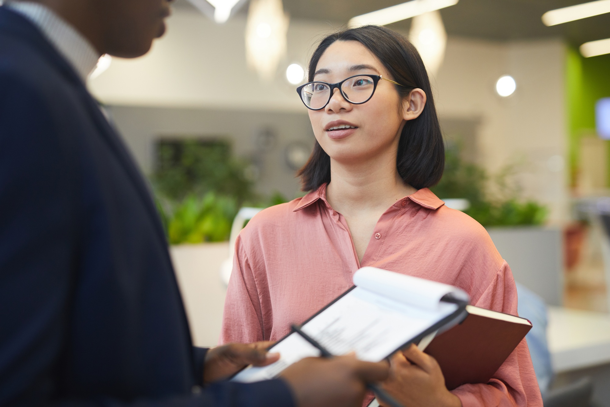 Portret młodej azjatyckiej bizneswoman rozmawiającej z partnerem podczas omawiania projektu pracy w nowoczesnym biurze od pasa w górę